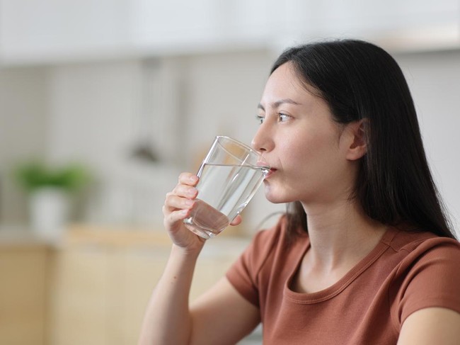 Asian woman drinking tap water from glass in the kitchen