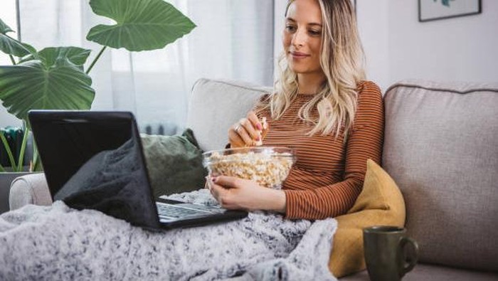 Young woman using a laptop in house. She is sitting on sofa and working on laptop.