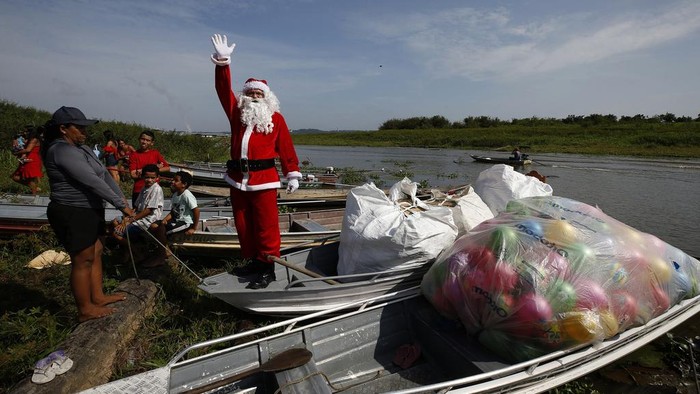 Jorge Barroso, dressed as Santa Claus, waves as he arrives on a boat to distribute Christmas gifts to children who live in the riverside communities of the Amazon, in Iranduba, Brazil, Saturday, Dec. 21, 2024. (AP Photo/Edmar Barros)