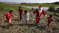 Di perahu yang lebih kecil, keluarga dari masyarakat tepi sungai terdekat lainnya juga diundang untuk menerima hadiah Natal langsung dari Sinterklas. 