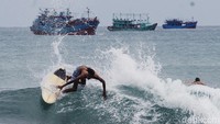 Aksi peselancar menaklukan ombak di Pantai Batu Karas. Latar kapal nelayan membuat suasana khas Pangandaran kian terasa.