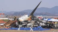 Petugas pemadam kebakaran dan anggota tim penyelamat bekerja di dekat puing pesawat penumpang di Bandara Internasional Muan di Muan, Korea Selatan, Minggu (29/12/2024).