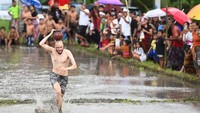 Wisatawan mancanegara berlari sambil menjunjung tembikar saat mengikuti lomba permainan tradisional di area persawahan Desa Suwat, Gianyar, Bali, Senin (30/12/2024).  