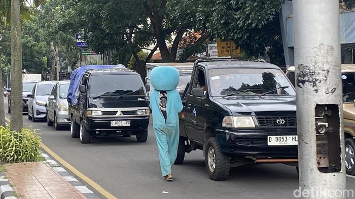 Hendrik (24) mengenakan kostum Doraemon tengah bekerja mencari uang di Perempatan Patung Husein Sastranegara, Kota Bandung. Kamis (26/12/2024).