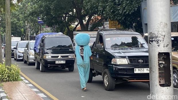 Hendrik (24) mengenakan kostum Doraemon tengah bekerja mencari uang di Perempatan Patung Husein Sastranegara, Kota Bandung. Kamis (26/12/2024).