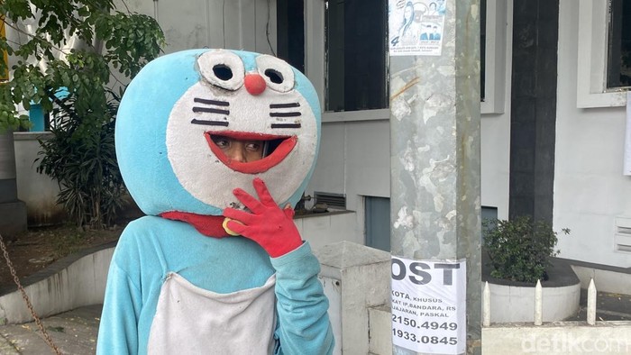 Hendrik (24) mengenakan kostum Doraemon tengah bekerja mencari uang di Perempatan Patung Husein Sastranegara, Kota Bandung. Kamis (26/12/2024).