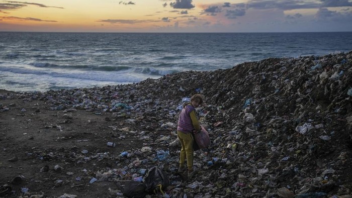 People walk along the beach next to a tent refugee camp for displaced Palestinians in Deir al-Balah, central Gaza Strip, Monday, Dec .30, 2024. (AP Photo/Abdel Kareem Hana)