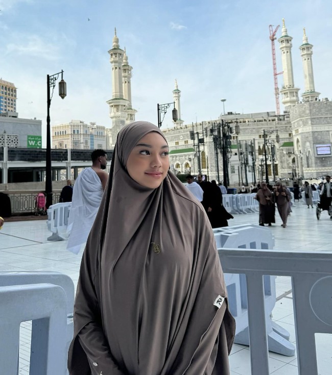 Pelantun Katakanlah Cinta itu berpose di depan Masjidil Haram dengan memakai setelan hijab syari dan dress.  Foto: Dok. Instagram @naura.ayu.