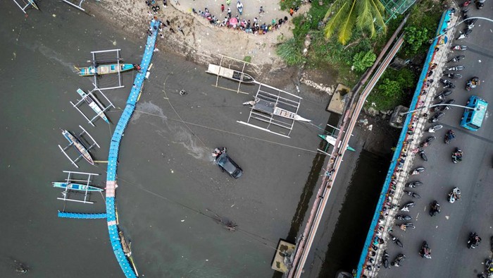 Foto udara sejumlah warga menyaksikan proses evakuasi mobil yang terjun ke sungai di Jembatan Megawati, Manado, Sulawesi Utara, Kamis (2/1/2025). Kecelakaan yang disebabkan kelalaian pengemudi tersebut mengakibatkan mobil terperosok ke sungai dan tidak ada korban jiwa.
