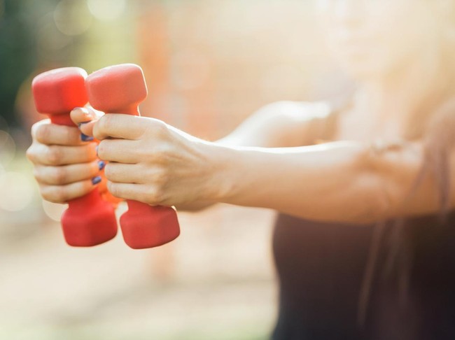 Girl making exercises with dumb-bells in the park. Shalow depth of field.