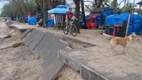 Wisatawan bersepeda di area pedestrian yang rusak akibat hempasan ombak di Pantai Kuta, Badung, Bali, Senin (6/1/2025).