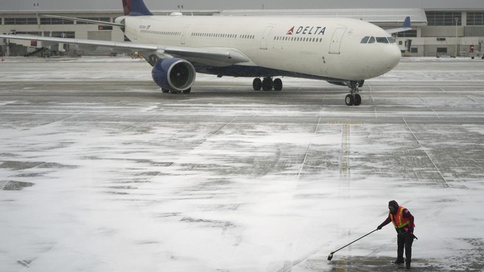 A worker clears snow from an apron before guiding a Delta Air Lines jet at the Detroit Metropolitan Wayne County Airport in Romulus, Mich., Monday, Jan. 6, 2025. (AP Photo/Charlie Riedel)