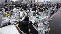 Mereka berusaha menghangatkan diri dengan selimut darurat saat berunjuk rasa di tengah badai salju.  
