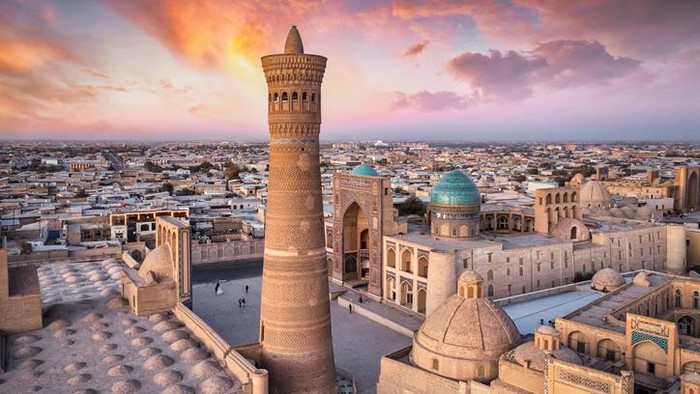 Colorful sunset twilight over the famous old town in the City of Bukhara with the iconic Kalyan Minaret and Mir-i-Arab Madressa. Aerial Drone Point of View. Itchan Kala, Bukhara, Khorezm Region, Uzbekistan, Central Asia.