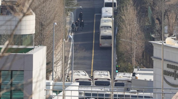 Security personnel walk on a road lined up with buses blocking the entrance gate of impeached South Korean president Yoon Suk Yeols residence in Seoul, South Korea, Wednesday, Jan. 8, 2025. (AP Photo/Ahn Young-joon)