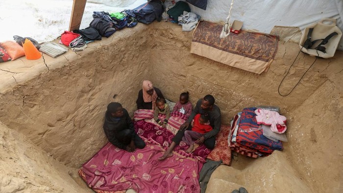 Pengungsi Gaza Bikin Lubang Bawah Tenda untuk Berlindung dari Serangan Israel Displaced Palestinian man Tayseer Obaid sits with his family in an underground pit he dug at their tent encampment to protect them from Israeli strikes, in Deir Al-Balah, central Gaza Strip, January 6, 2025. REUTERS/Ramadan Abed TPX IMAGES OF THE DAY