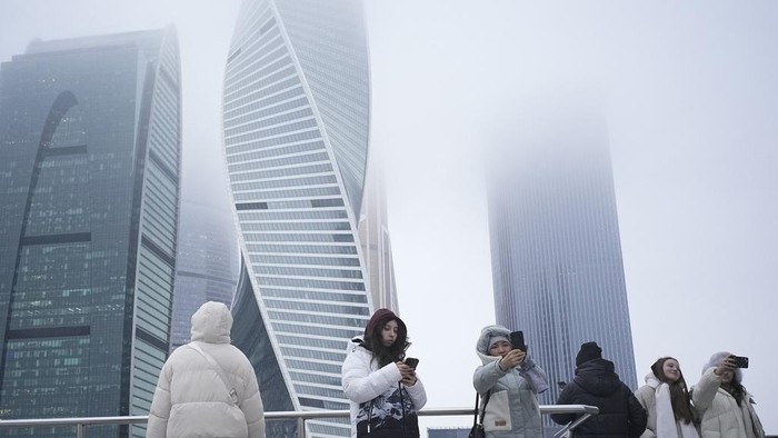People take selfies with the skyscrapers of the Moscow City business district in the background on a foggy day in Moscow, Russia, Tuesday, Jan. 7, 2025. (AP Photo/Pavel Bednyakov)