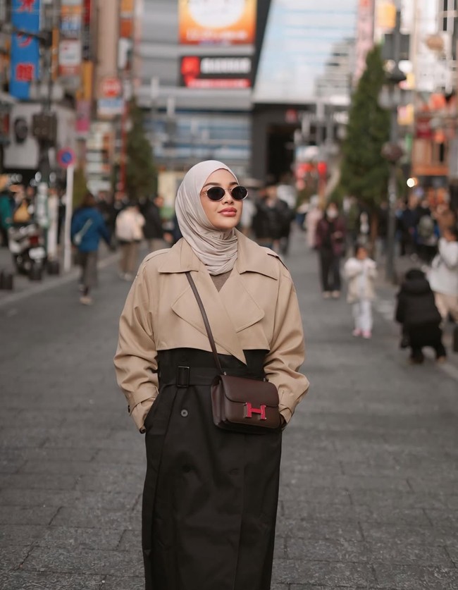 Di kesempatan lain wanita 26 tahun itu memilih mengenakan long coat two tone berwarna coklat dan hitam. Ia kemudian memadukan penampilannya dengan hijab berwarna coklat muda dan kaca mata hitam. Tas selempang berwarna coklat tua dari merek mewah Hermes juga terlihat menggantung di pundaknya. Foto: Instagram/@aurelie.hermansyah