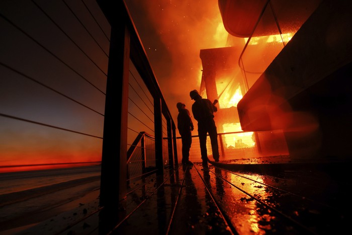 Firefighters work from a deck as the Palisades Fire burns a beach front property Wednesday, Jan. 8, 2025 in Malibu, Calif. (AP Photo/Etienne Laurent)