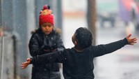 Anak-anak bermain di bawah hujan salju.  