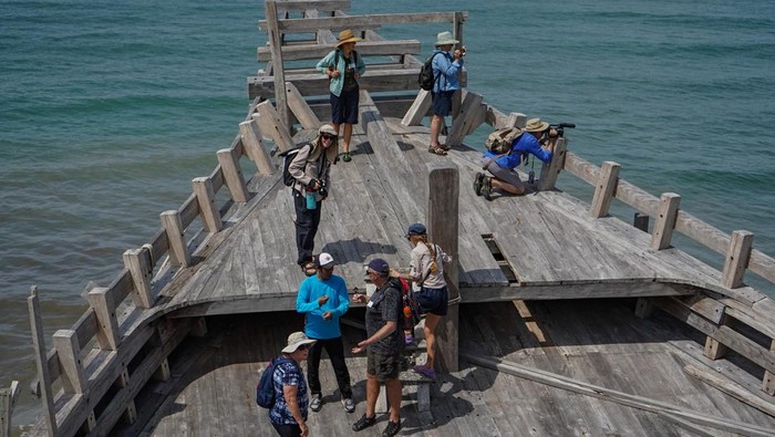 Wisatawan mancanegara menyaksikan proses pembuatan kapal Pinisi di Tanah Beru, Kabupaten Bulukumba, Sulawesi Selatan, Jumat (10/1/2025). Puluhan turis dari berbagai negara tersebut datang untuk mengenal lebih dekat warisan budaya maritim Indonesia yang telah diakui UNESCO sebagai warisan budaya takbenda, sekaligus menyaksikan langsung keahlian para pengrajin lokal dalam membangun kapal secara tradisional menggunakan pasak kayu. ANTARA FOTO/Hasrul Said/foc.