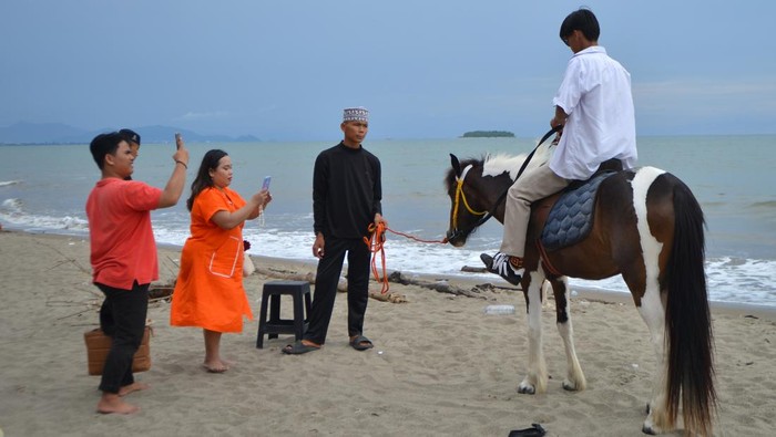 Santri memandu pengunjung yang menyewa jasa kuda wisata di Pantai Pasir Jambak, Padang, Sumatera Barat, Minggu (12/1/2025). Santri dari pondok pesantren Kanzul Ulum Padang itu menyewakan jasa berkuda dengan tarif Rp40 ribu per orang dan Rp10 ribu per orang untuk berfoto, dalam rangka menjalankan program kemandirian yang didukung Kementerian Agama dalam menunjang ekonomi pesantren meliputi inovasi perekonomian untuk para santri dan masyarakat sekitar. ANTARA FOTO/Iggoy el Fitra/nym.