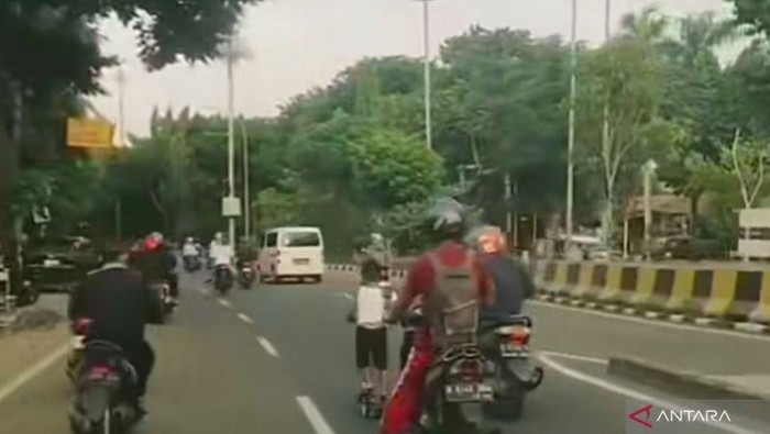 Seorang anak bermain skuter di tengah jalan raya depan Kantor Walikota Madya Jakarta Timur.