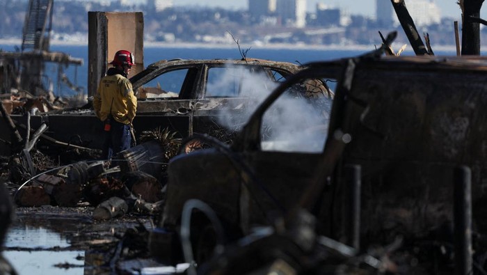 A firefighter stands near burnt vehicles following the Palisades Fire along Pacific coast in Malibu, California, U.S.  January 13, 2025. REUTERS/Mike Blake