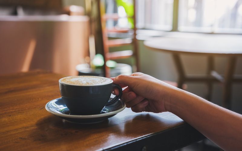 Closeup image of a hand holding coffee cup on wooden table