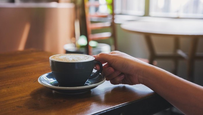 Closeup image of a hand holding coffee cup on wooden table
