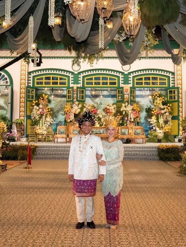 Di akad nikahnya, Erlangga tampil mengenakan busana adat berwarna putih dipadukan dengan kain berwarna keunguan seperti yang dikenakan oleh Sekar. Pakaian tersebut dilengkapi dengan penutup kepala berwarna hitam dengan aksen keemasan. Melengkapi penampilannya, Erlangga juga mengenakan aksesori seperti kalung berwarna emas. Foto: Instagram/@sekar.tandjung