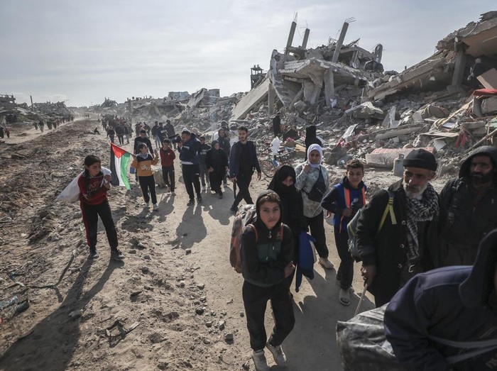 Palestinians walk through the destruction caused by the Israeli air and ground offensive in Jabaliya, as a ceasefire deal between Israel and Hamas went into effect, Sunday, Jan. 19, 2025. (AP Photo/Abed Hajjar)