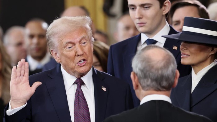Detik-detik Trump Resmi Kembali Menguasai AS President-elect Donald Trump, from left, takes the oath of office as son Barron Trump and wife Melania Trump watch during the 60th Presidential Inauguration in the Rotunda of the U.S. Capitol in Washington, Monday, Jan. 20, 2025. (Kevin Lamarque/Pool Photo via AP)