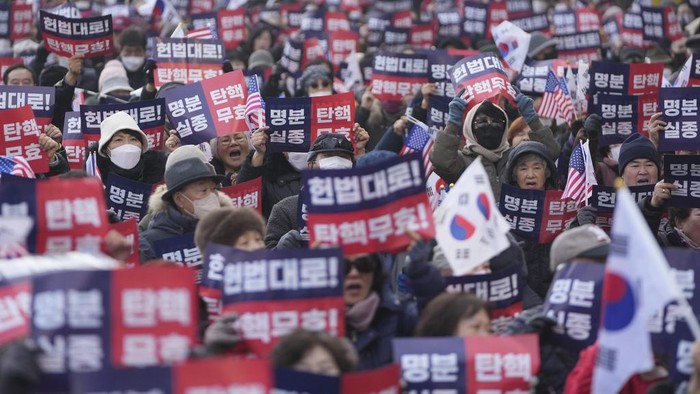 Supporters of impeached South Korean President Yoon Suk Yeol gather as police officers block the road to the Constitutional Court in Seoul, South Korea, Tuesday, Jan. 21, 2025. The letters read 
