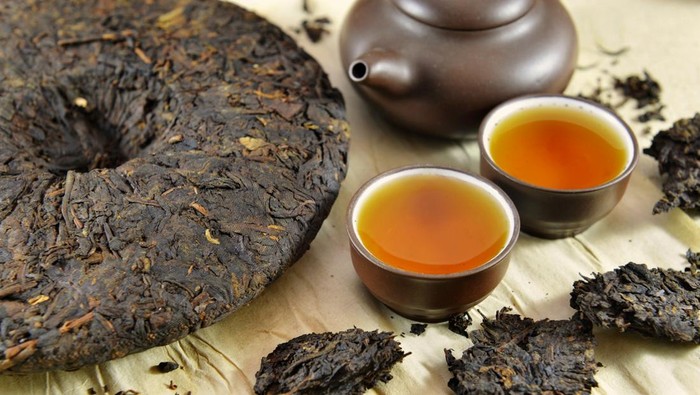 Still life with Asian pressed pu-erh tea and crockery tea set, clay pot and two small cups full of hot tea, on paper background