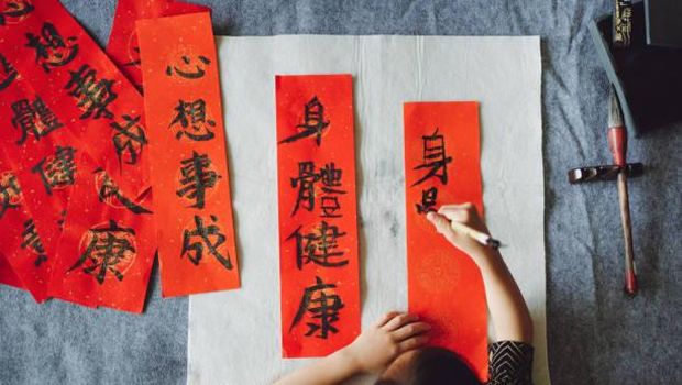 Top view of Asian little girl practicing Chinese calligraphy for Chinese New Year Fai Chun (Auspicious Messages) .