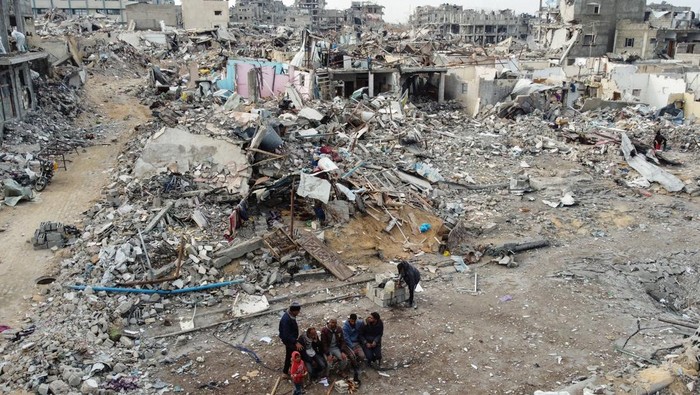 Palestinians sit near the rubble of buildings destroyed during the Israeli offensive, following a ceasefire between Israel and Hamas, in Rafah in the southern Gaza Strip, January 22, 2025. REUTERS/Mohammed Salem     TPX IMAGES OF THE DAY