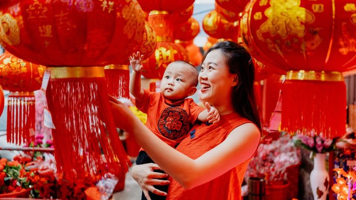 An Asian Chinese mother carrying her baby shopping and looking for red lantern for Chinese new year decoration