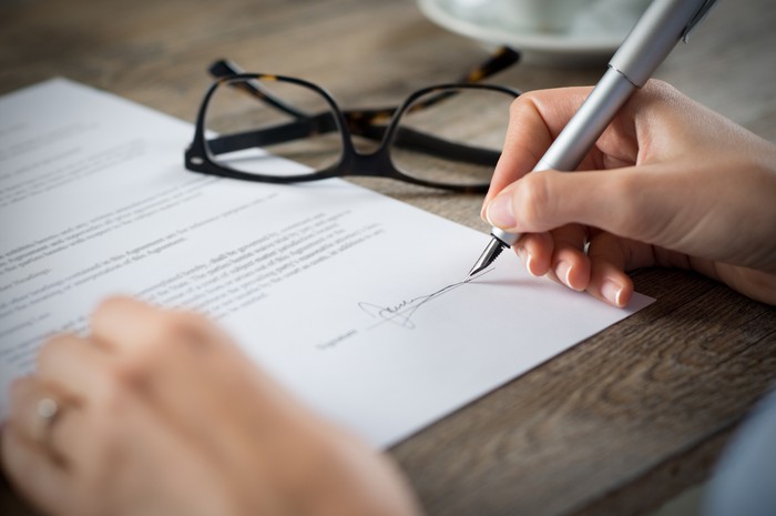 Closeup shot of a woman signing a form. Shes writing on a financial contract. Shallow depth of field with focus on tip of the pen.