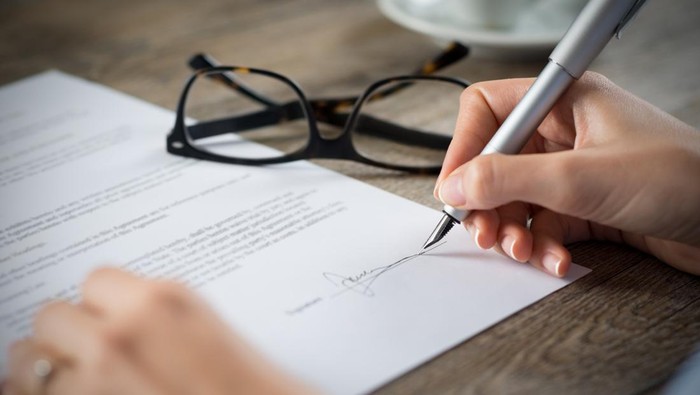 Closeup shot of a woman signing a form. Shes writing on a financial contract. Shallow depth of field with focus on tip of the pen.