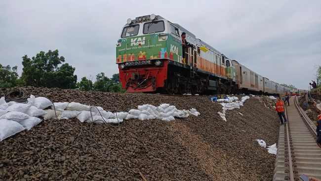 Kereta api melintas dengan kecepatan terbatas di jalur rel yang tergerus banjir di Kabupaten Grobogan, Jumat (24/1/2025) pagi.