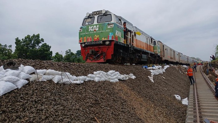 Kereta api melintas dengan kecepatan terbatas di jalur rel yang tergerus banjir di Kabupaten Grobogan, Jumat (24/1/2025) pagi.