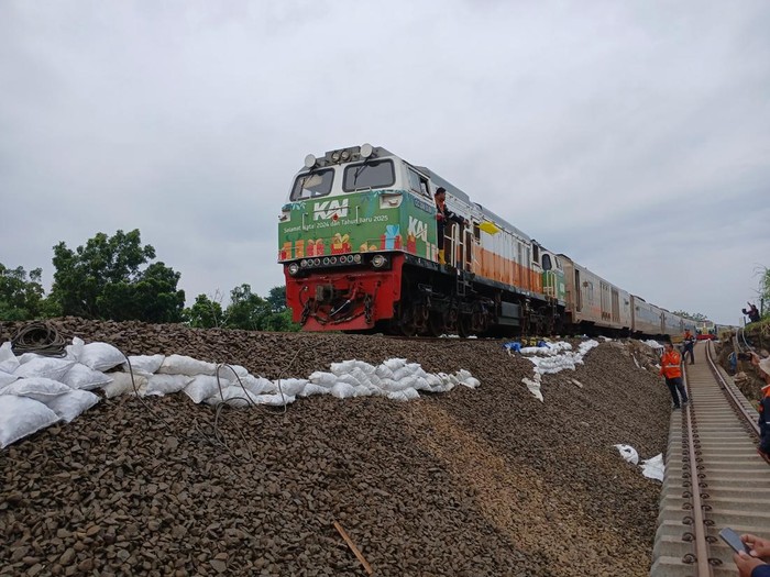 Kereta api melintas dengan kecepatan terbatas di jalur rel yang tergerus banjir di Kabupaten Grobogan, Jumat (24/1/2025) pagi.