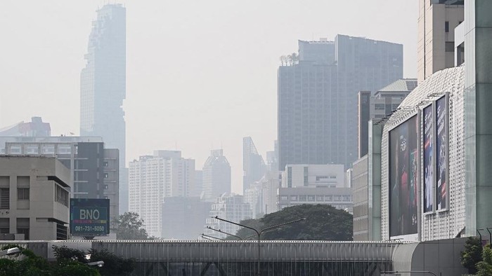 People are seen walking through a pedestrian bridge amidst high levels of air pollution in Bangkok on January 24, 2025. (Photo by Lillian SUWANRUMPHA / AFP)