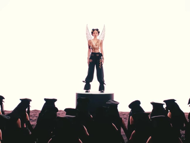 Tak kalah ikonik. Jennie BLACKPINK mereplikasikan model rambut ala Ratu Korea, lengkap dengan hair piece bernuansa gold. Dia memakai ornamen sayap yang terkesan dramatis sebagai atasannya, rancangan desainer lokal LEJE. Foto: dok. YouTube JENNIE