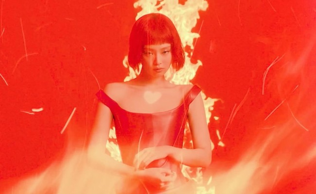 Tampil fearless di depan kobaran api. Warna merah seolah menjadi statement album Jennie yang dirilis pada 7 Maret 2025. Dia memakai Leather Corset Draped Mini Dress dari rumah mode Italia Versace seharga US$8,575 atau Rp 140 juta. Foto: dok. YouTube JENNIE