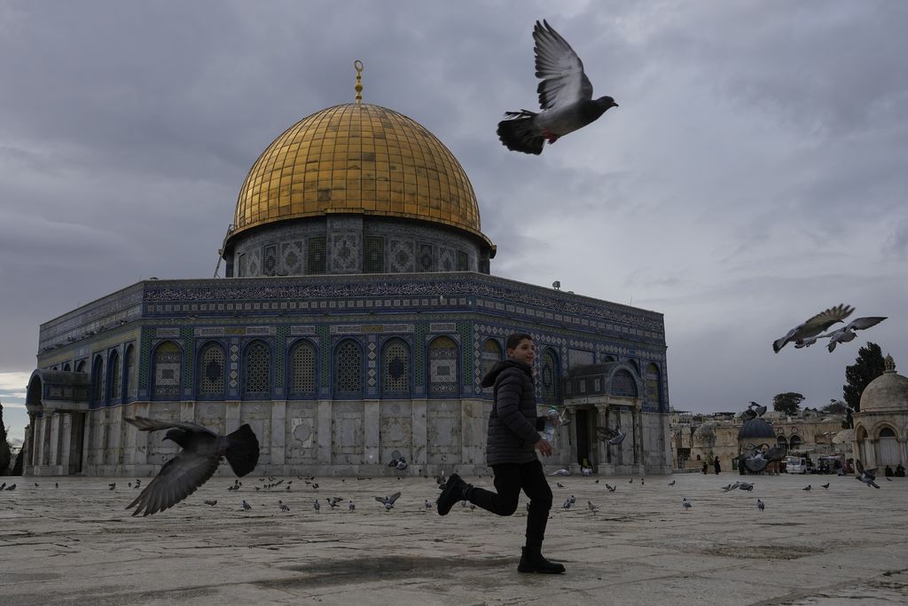 A boy runs amid pigeons flying next to the Dome of Rock Mosque at the Al-Aqsa Mosque compound in Old City of Jerusalem, Monday, Dec. 30, 2024. (AP Photo/Matias Delacroix)