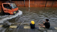 Anak-anak juga asyik bermain air sambil melihat kendaraan menerobos banjir.