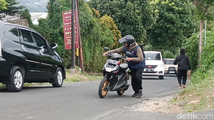 Pengendara mendorong sepeda motornya yang menyerah melintas di Tanjakan Naga Lembang.