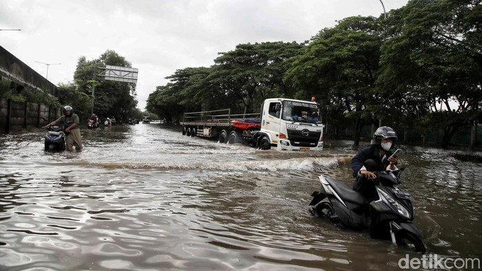 Sejumlah warga menerobos banjir di kawasan Jalan Raya Cakung Cilincing, Jakarta Utara, Kamis (30/1/2024).